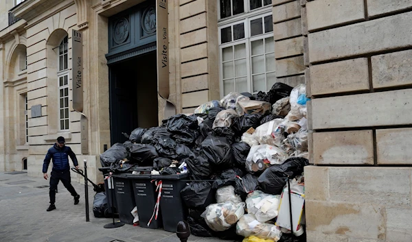 A man walks past uncollected garbages in Paris, Friday March 17, 2023 (AP)