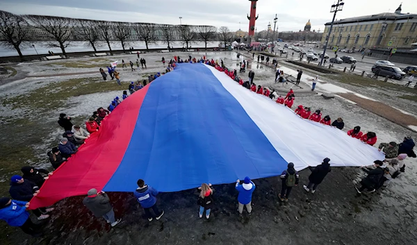 Young people unfurl a giant Russian flag during an action to mark the ninth anniversary of Crimea's reunification with Russia in St. Petersburg, Russia, March 18, 2023 (AP)