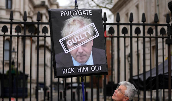 A protester holds a sign showing former British Prime Minister Boris Johnson as he stands in front of the entrance to Downing Street in London, Wednesday, April 13, 2022 (AP).