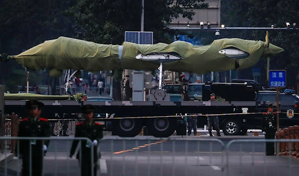 In this Saturday, Sept. 21, 2019, photo, Chinese paramilitary policemen patrol as a Chinese military vehicle possibly carrying a drone passes along the Jianguomenwai Avenue during a rehearsal for the 70th anniversary of Communist China, in Beijing.