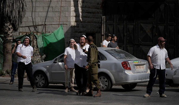 An Israeli occupation forces soldier talks with Israeli settlers during confrontations when the settlers attacked Palestinians in Huwara, near the occupied West Bank town of Nablus, occupied Palestine, October 13, 2022 (AP Photo)