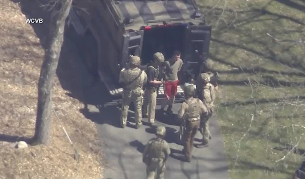 This image made from video provided by WCVB-TV, shows Jack Teixeira, in T-shirt and shorts, being taken into custody by armed tactical agents on Thursday, April 13, 2023, in Dighton, Mass. (WCVB-TV via AP)