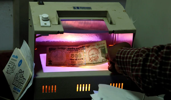 A banker checks an Indian currency note in a forgery detection machine at a bank in Allahabad, India, Friday, Dec. 16, 2011. (AP)