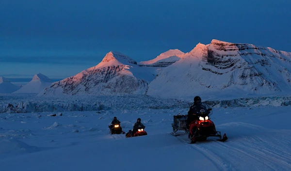 NPI (Norwegian Polar Institute) scientists ride their snowmobiles as the sun sets at the banks of Kongsfjord and the Kronebreen glacier near Ny-Aalesund, Svalbard, Norway, April 10, 2023. (Reuters)