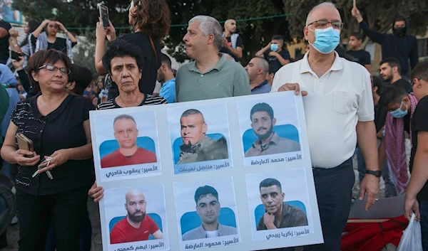 Protesters lift a placard depicting the six Palestinian prisoners who broke out from the Gilboa prison through operation Freedom Tunnel, as they demonstrate to support them in Al-Nasira, occupied Palestine, 11 September 2021 (AFP)