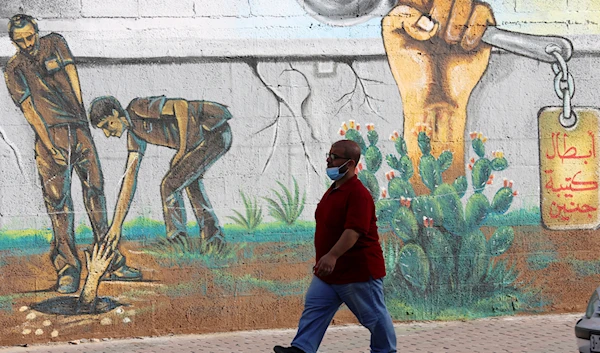 A resident walks next to a mural painting of the six Palestinian prisoners who reclaimed their freedom from the Israeli occupation through Operation Freedom Tunnel, in Gaza City, occupied Palestine, September 23, 2021 (AP)