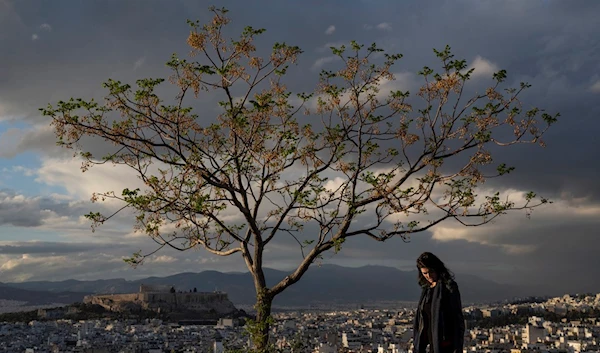 A woman walks with her dog as in the background is seen the city of Athens with the ancient Acropolis hill, left, on Tuesday, April 4, 2023 (AP Photo/Petros Giannakouris)