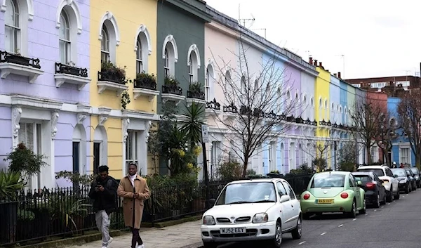 Two people walk alongside colorful houses in London, UK, 19 May 2023. (Reuters)