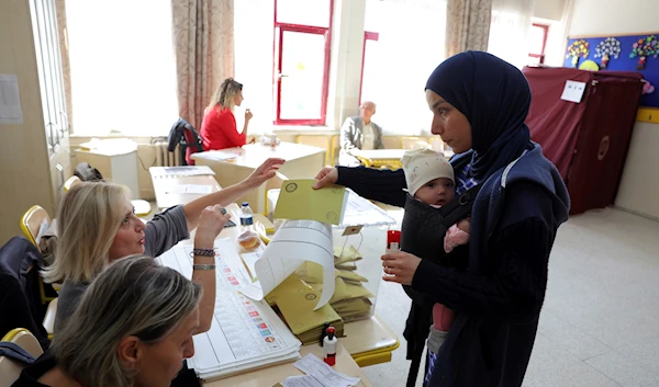 A woman with a baby takes a ballot at a polling station in Ankara, Turkey, Sunday, May 14, 2023 (AP Photo)