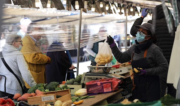 A produce vendor holds a plastic bag containing potatoes as she serves clients behind a plastic sheet at a street market in Paris, France, May 14, 2020. (AFP)