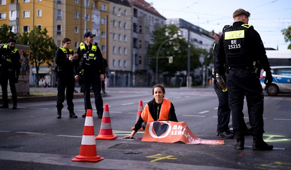 Police officers stand around a climate activist who has glued her hand on a street during a climate protest in Berlin, Germany, Friday, May 19, 2023. (AP)