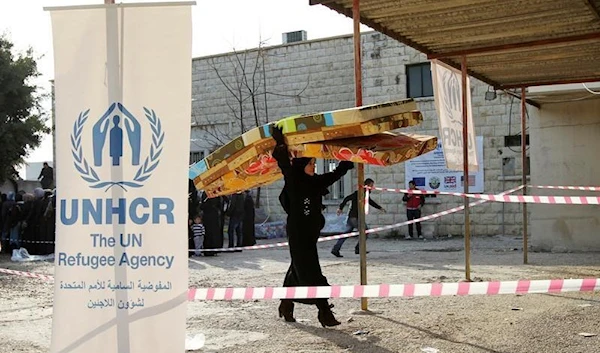 A Syrian refugee carries mattresses as she walks by a banner of the UNHCR at a camp in Batroun, Lebanon, May 13 2015. (Reuters)