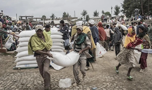 In this file photo taken on September 15, 2021, men carry a sack of wheat distributed by the World Food Program (WFP) for internally displaced people in Ethiopia. (AFP)