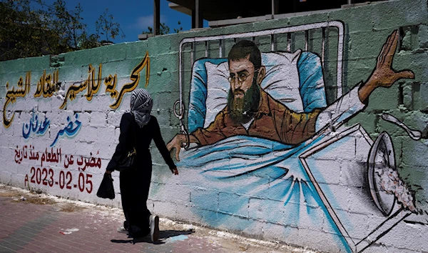 A Palestinian woman walks past a mural of Khader Adnan, a Palestinian Islamic Jihad militant who died in Israeli prison after a nearly three-month hunger strike, in Gaza City, Tuesday, May 2, 2023. (AP)