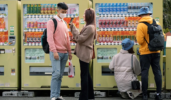 Tourists look at their photos in front of vending machines as they were visiting Sensoji Buddhist temple in Tokyo, Friday, Jan. 13, 2023. (AP)