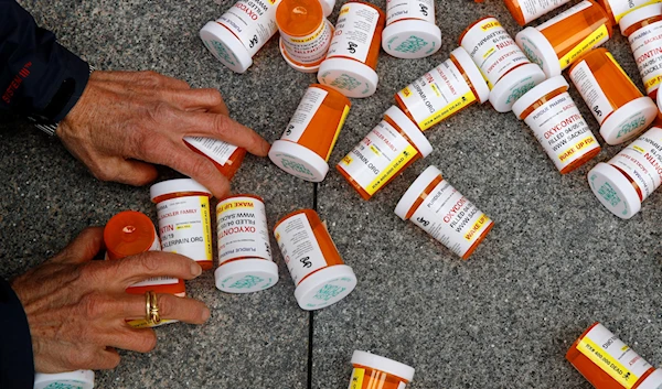 A protester gathers containers that look like OxyContin bottles at an anti-opioid demonstration in front of the US Department of Health and Human Services headquarters in Washington on April 5, 2019 (AP)