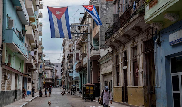 A man walks under Cuban flags flying over a street in Havana, Cuba, Monday, July 26, 2021 (AP Photo/Eliana Aponte)