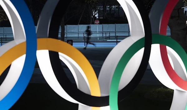 A man jogs past the Olympic rings Monday, March 30, 2020, in Tokyo. The Tokyo Olympics will open next year in the same time slot scheduled for this year's games. Tokyo organizers said Monday the opening ceremony will take place on July 23, 2021. (AP)