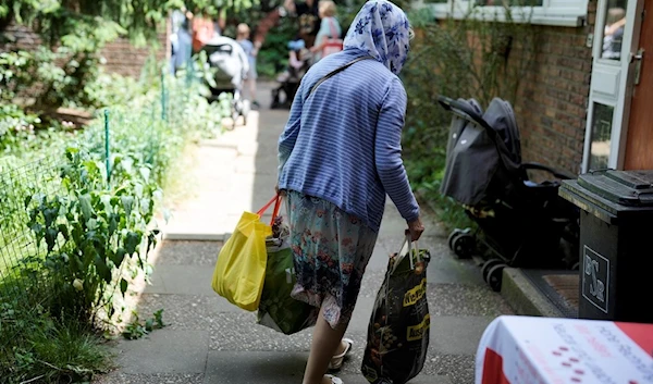 An elderly woman leaves a food distribution center with her bags, packed with groceries, at the Catholic St. William Church in Berlin, Germany, Wednesday, May 31, 2023 (AP Photo/Markus Schreiber)