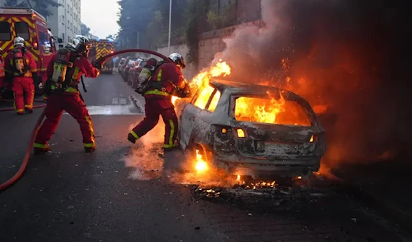 Firefighters work to put out a burning car on the sidelines of a demonstration in Nanterre, west of Paris, on June 27, 2023, after police killed a teenager who refused to stop for a traffic check. (AFP)