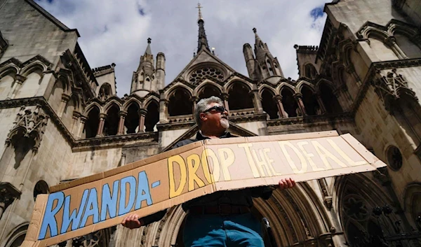 A demonstrator holds a placard during a protest against Britain's Rwanda asylum plan outside the High Court in London on June 13, 2022 (AFP)