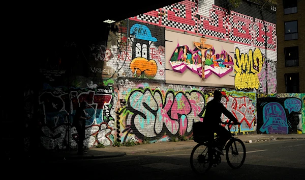 A man cycles past graffiti on in the Tower Hamlets neighborhood in London, Friday, July 22, 2022. (AP)