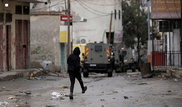 A Palestinian throws rocks at Israeli military vehicles raiding Aqbat Jabr camp, southwest of the city of Jericho on Saturday, Feb. 4, 2023. (AP)