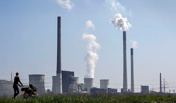 A mother pushes a stroller in front of the Scholven coal-fired power station, owned by Uniper, in Gelsenkirchen, Germany, March 28, 2022 (AP)