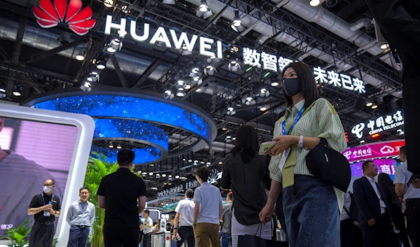 Visitors wearing face masks walk past a display from Chinese technology company Huawei at the PT Expo in Beijing, China, June 4, 2023 (AP)