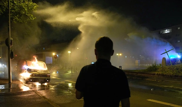 Firefighters use a water hose on a burnt car in Nanterre, outside Paris, France, Saturday, July 1, 2023 (AP Photo/Lewis Joly)