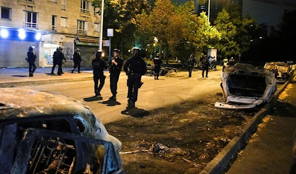 Police officers pass by charred cars in Nanterre, outside Paris, France, Saturday, July 1, 2023 (AP Photo/Lewis Joly)