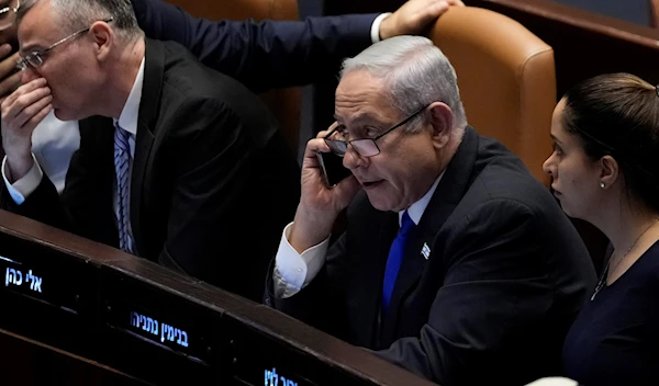 Israeli Occupation Prime Minister Benjamin Netanyahu speaks on a mobile phone as he sits at the Knesset, in Al-Quds, Monday, July 10, 2023. (AP)