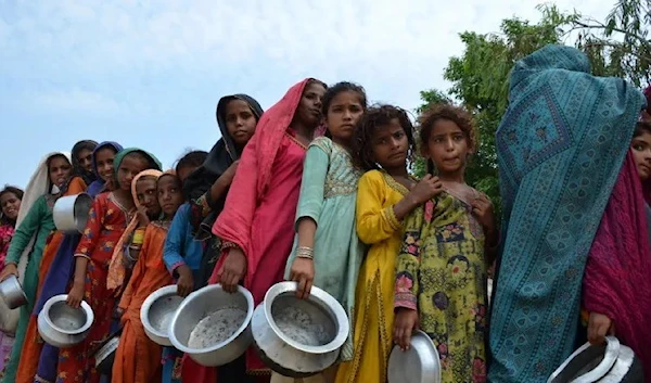 People wait receiving food that Saylani Welfare Trust distributed at a makeshift camp in Sehwan, Sindh province, Pakistan, on September 2022. (AFP)