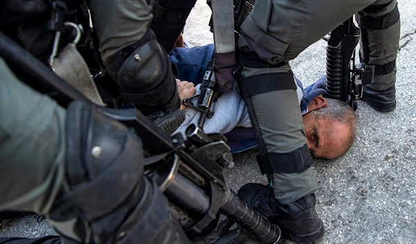 Israeli troops detain a Palestinian man after Israeli settlers blocked Palestinian children from entering a school in the village of al Lubban al Sharqiya, near the West Bank city of Nablus, Occupied Palestine, Sunday, Nov. 28, 2021.(AP)