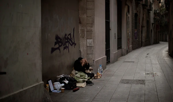 In this Saturday, March 21, 2020 photo, Javier Redondo, 40, covers his head with his hands as he waits for alms on an empty street in Barcelona, Spain. (AP)