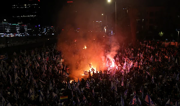 Israelis opposed to Prime Minister Benjamin Netanyahu's judicial overhaul plan set up bonfires and block a highway during a protest moments after the Israeli leader fired his defense minister, in 'Tel Aviv', occupied Palestine, March 26, 2023 (AP)