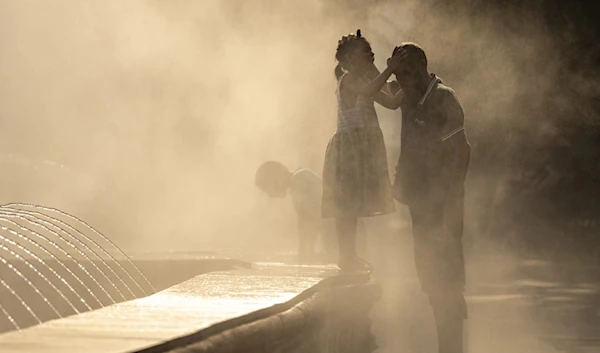 A little girl touches her father’s head as they are engulfed by mist from a public fountain in Bucharest, Romania Thursday, July 13,2023. (AP)