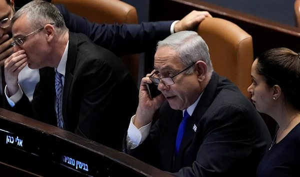 Israeli occupation Prime Minister Benjamin Netanyahu speaks on a mobile phone as he sits at the Knesset in occupied Al-Quds, July 10, 2023 (AP)