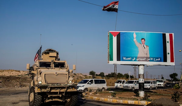 In this October 26. 2019 file photo, US military convoy drives in the town of Al Qamishli, northern Syria, by a poster depicting Syrian President Bashar Aassad. (AP)