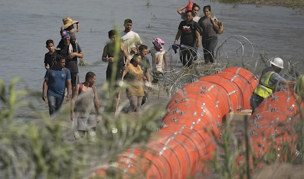 Migrants trying to enter the US from Mexico approach the site where workers are assembling large buoys to be used as a border barrier along the banks of Rio Grande, in Texas, on July 11, 2023. (AP)