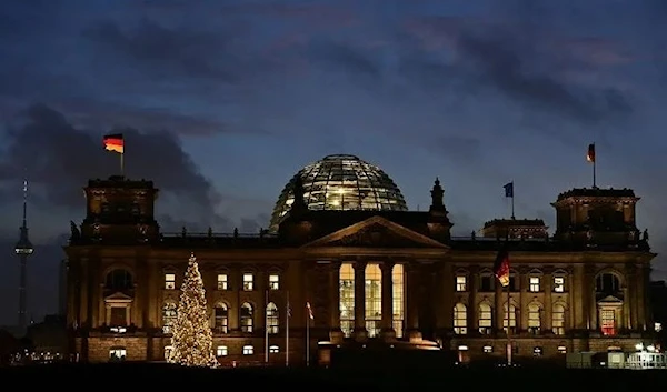 A German flag flutters on the Reichstag building that houses the Bundestag (lower house of parliament) in Berlin is illuminated on early December 8, 2021. (AFP)