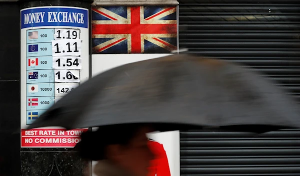 A pedestrian with an umbrella passes a board showing the exchange rates at a money exchange bureau in London, Monday, Jan. 16, 2017. (AP)