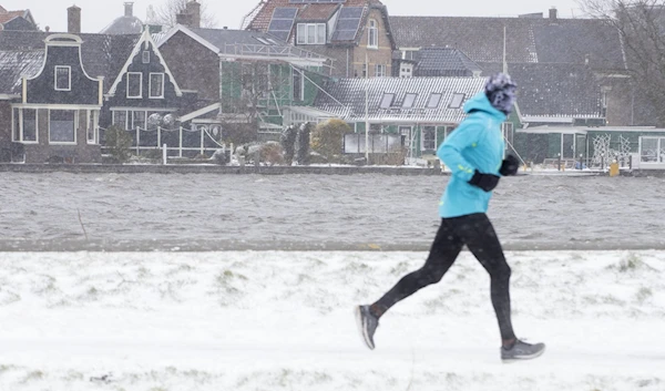 A man exercises along Zaanse Schans river in Zaandam, as snow and strong winds blanketed the Netherlands, Sunday, Feb. 7, 2021. (AP)