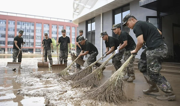 In this photo released by Xinhua news agency, members of the armed police force clean up sludge left after the flood caused by the rainstorms brought by Typhoon Doksuri