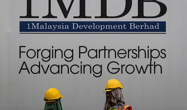 In this May 14, 2015 photo, construction workers chat in front of a billboard for state investment fund 1 Malaysia Development Berhad (1MDB) in Kuala Lumpur, Malaysia (AP)