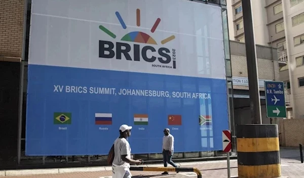 People walk past a banner outside the venue for the 2023 BRICS Summit at the Sandton Convention Centre in Sandton, Johannesburg, on August 20, 2023. (AFP)