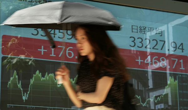 A woman walks past monitors showing Japan's Nikkei 225 index at a securities firm in Tokyo, July 31, 2023 (AP)