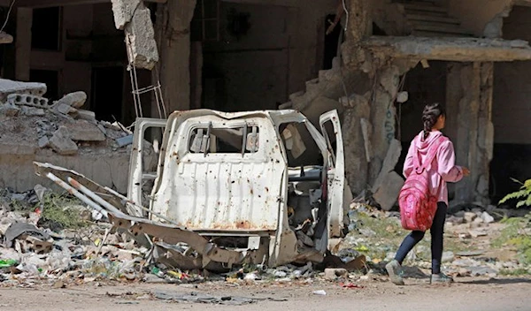 A young girl walks past a damaged vehicle and destroyed building in the southern suburbs of Damascus on Nov. 2, 2022. (AFP)