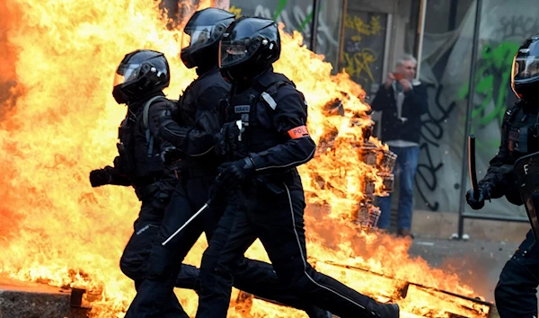 French riot police run past a fire during a demonstration in Paris on March 23, 2023 (AFP)