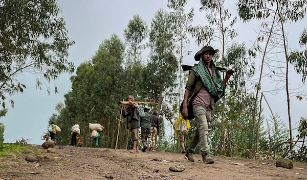 An unidentified armed militia fighter walks down a path as villagers flee with their belongings in the other direction, near the village of Chenna Teklehaymanot, in the Amhara region of northern Ethiopia Thursday, Sept. 9, 2021. (AP)